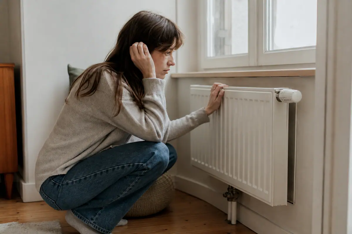 Main tenant une clé de purge devant un radiateur en fonte dans un salon lumineux