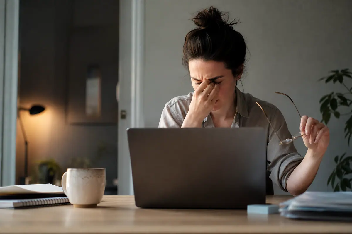 Personne se frottant les yeux devant un ordinateur en fin de journée dans un bureau