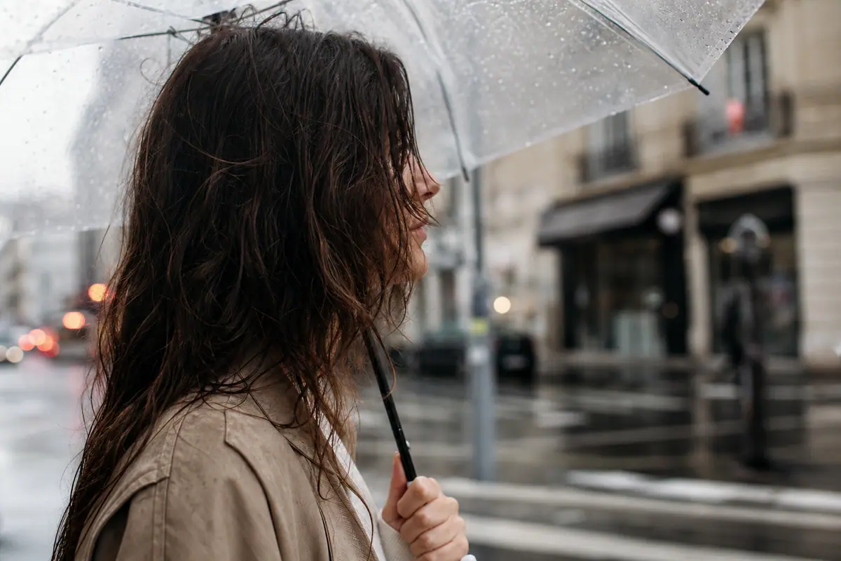 Femme sous la pluie touchant ses cheveux frisottés dans une rue