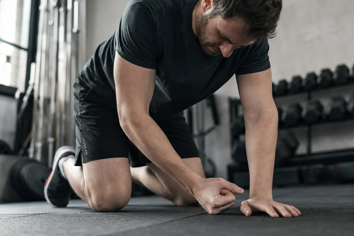Personne en position de pompe au sol, poignets en appui, dans une salle de sport lumineuse