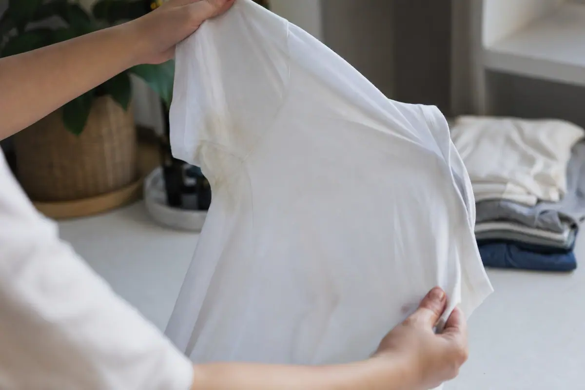 Mains tenant un t-shirt blanc marqué d'une auréole jaunâtre sous le bras