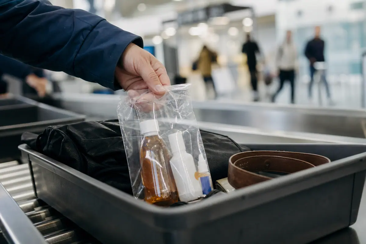 Main déposant un sachet transparent de flacons de médicaments dans un bac au contrôle de sûreté d'un aéroport