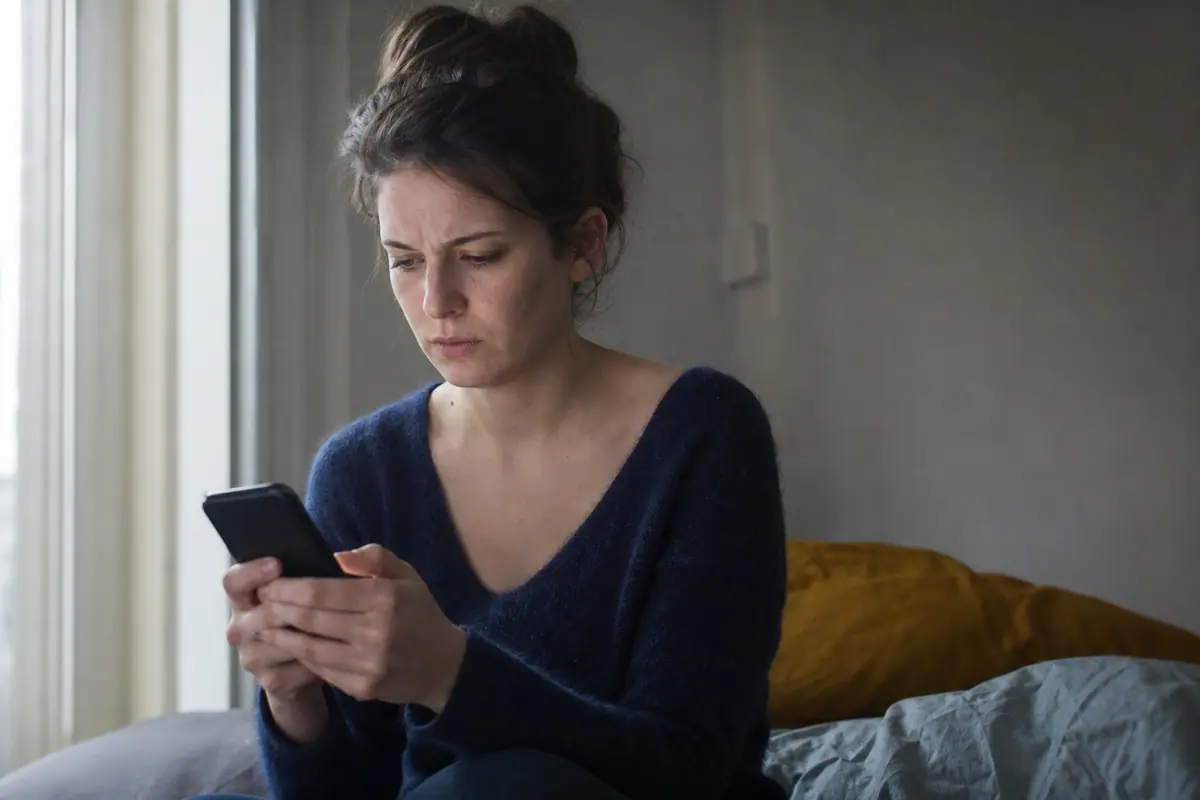 Personne assise sur un lit, l'air méfiant, lisant des messages sur son téléphone